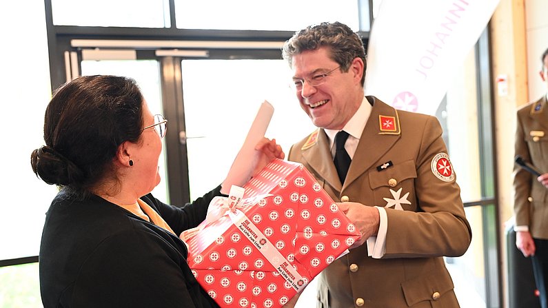 Auf dem Bild sind zwei Personen zu sehen. Eine Person erhält ein Geschnek. 