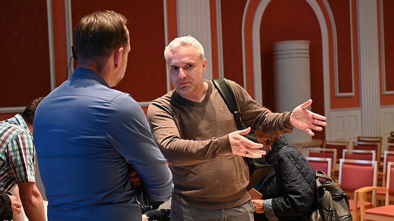 Auf dem Foto sind zwei Personen zu sehen (männlich), die sich unterhalten. 