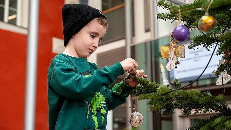 Auf dem Bild ist ein Kind zu sehen, welches auf einer Leiter steht und einen Weihnachtsbaum schmückt.