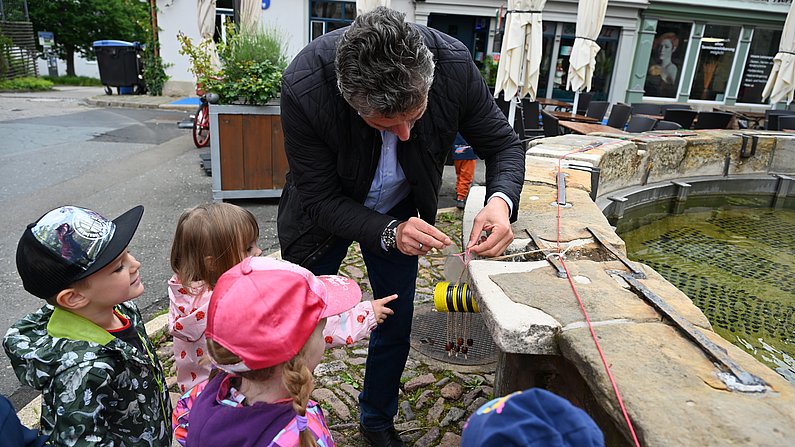 Auf dem Bild sind Kinder und Bürgermeister Frank Spilling beim Brunnen schmücken zu sehen. 