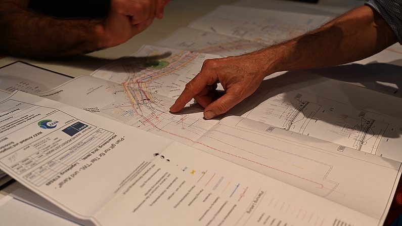 Auf dem Foto ist eine Hand auf einem Bauplan zu sehen. 