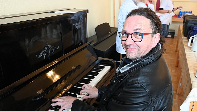 Auf dem Foto sieht man einen lächelnden Mann am Klavier. 