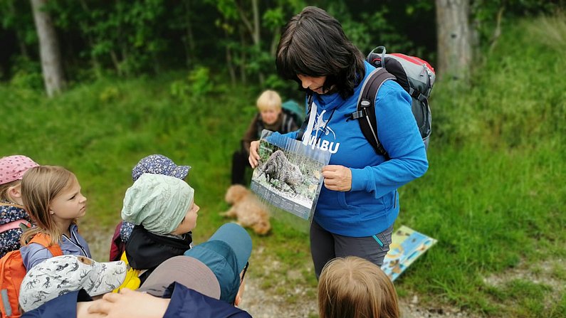 Auf dem Bild ist eine Frau von der NABU zu sehen, die Kindern Biberschäden erklärt. 