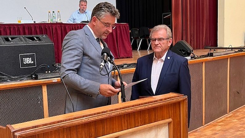 Zwei Männer stehen an einem Pult und unterhalten sich.